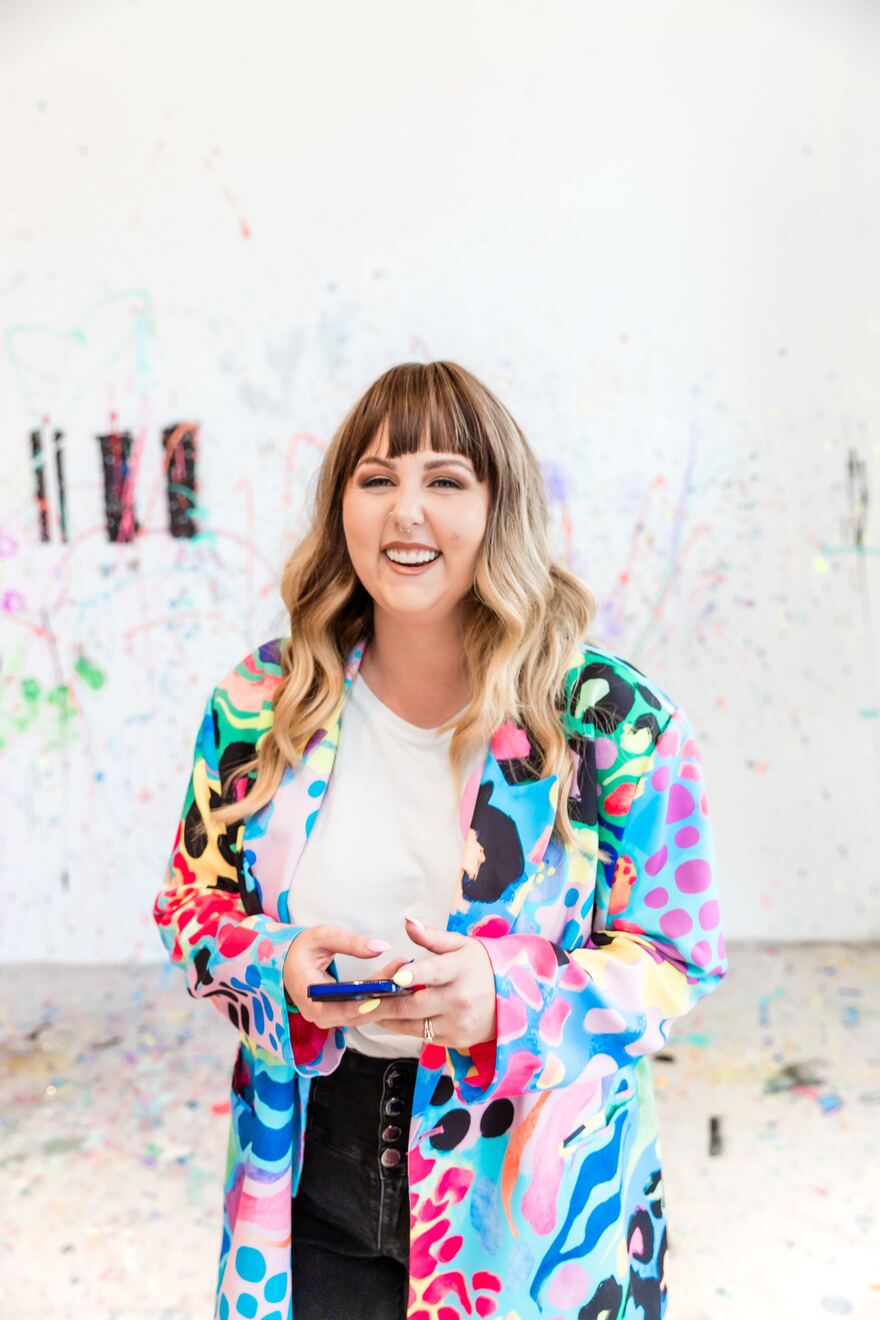 Kayla, founder of That Socials Team, in a colourful jacket holding her phone